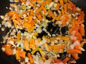 Orange bell peppers, onions, and mushrooms softening in the pan